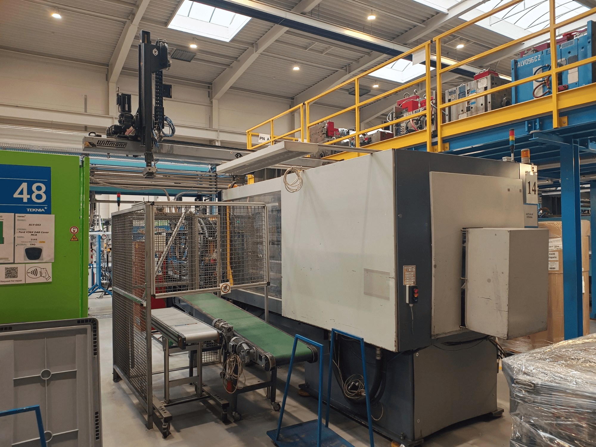 Teollisuusautomaatiolaitteisto, jossa on vihreä kuljetin, jossa on merkintä "48", ja nosturi; sivukuva koneesta tehtaan lattialla.